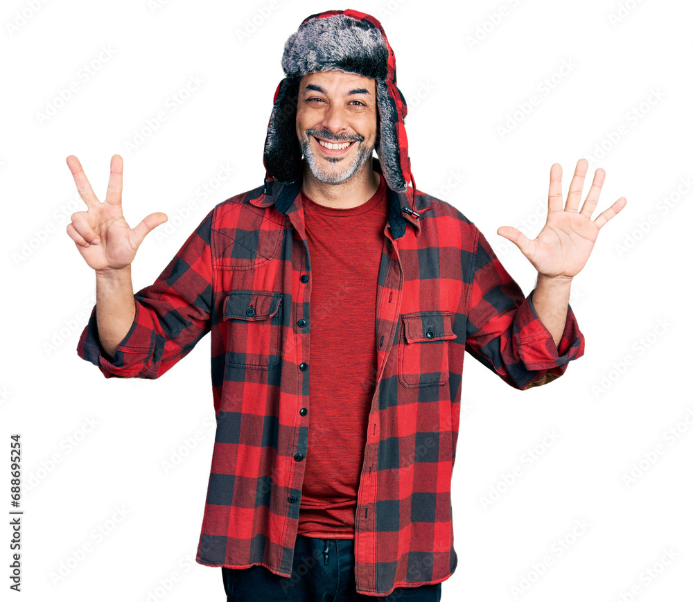 Sticker middle age hispanic man with grey hair wearing fluffy earmuff hat showing and pointing up with finge