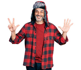 Middle age hispanic man with grey hair wearing fluffy earmuff hat showing and pointing up with fingers number eight while smiling confident and happy.