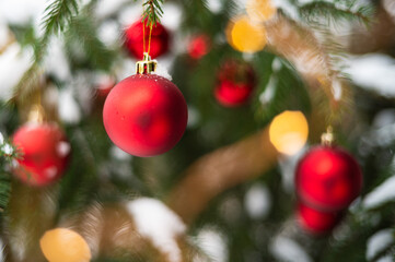 Red baubles on a snow-covered Christmas tree outdoors