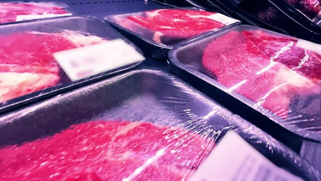 Raw beef steaks in plastic containers covered with cling-wrap in a supermarket fridge. Close-up
