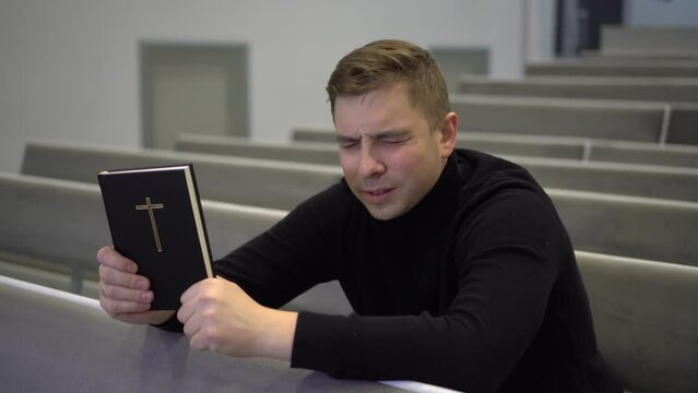 A young man prays holding a bible in his hands
