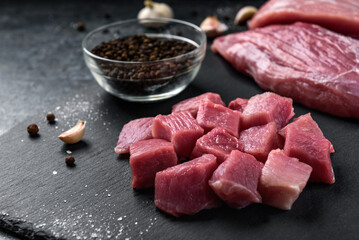 Diced raw pork meat with on slate board on black background.