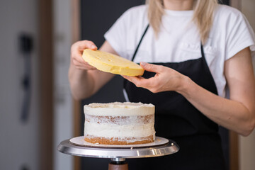 Professional confectioner in black apron connecting gluten free cake layers smeared with white...