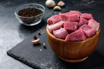 Diced raw pork meat in wooden bowl on black background.