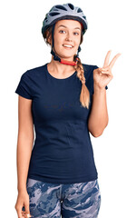 Beautiful caucasian woman wearing bike helmet showing and pointing up with fingers number two while smiling confident and happy.