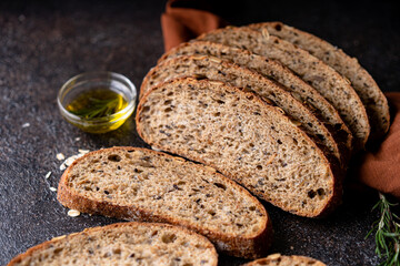 Sliced sourdough bread from whole grain flour and pumpkin seeds on a grid, olive oil and black olive on a rustic wooden table. Artisan bread.