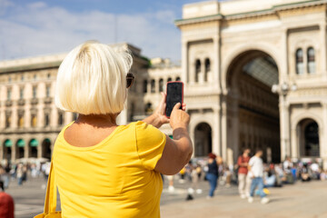 Beautiful senior blonde woman taking selfie on Duomo square, Galleria Vittorio Emanuele II shopping...
