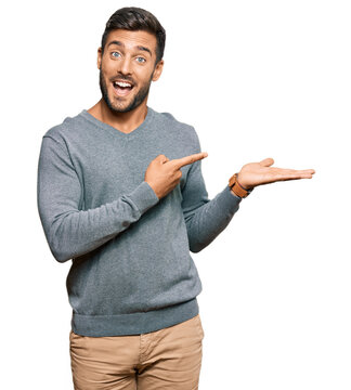 Handsome hispanic man wearing casual clothes amazed and smiling to the camera while presenting with hand and pointing with finger.