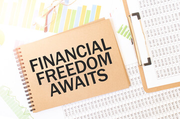 Business up graph on a sheet of craft colour Notepad with FINANCIAL FREEDOM AWAITS sign. Notepad on desk with financial documentation