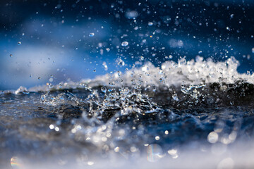 Water splashing into a rain barrel rimmed with ice crystals. Vivid water surface with drops,...