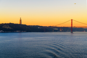 Sunset view of the Sanctuary of Christ the King monument and statue looking over the Tagus River and the Ponte 25 de Abril bridge from the Alfama district in Lisbon, Portugal.