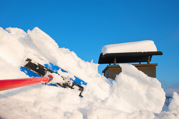 remove a lot of snow from the roof window with the snow shovel. blue sky and chimney