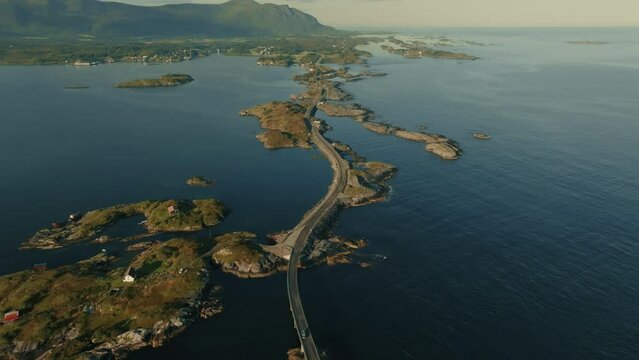 Drone zooms out to reveal Atlantic Ocean road, connecting small islands in vast blue sea in bright sunlight