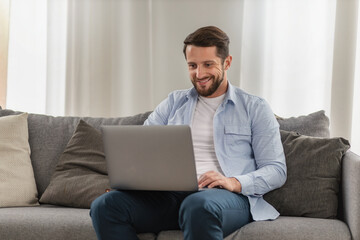 Man entrepreneur seamlessly blending work and home life as he tackles business tasks online using laptop from the comfort of his living room at home