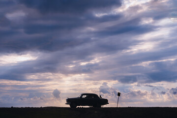 Silhouette of a retro vehicle standing on the beach. Stormy sea in the background, big waves, Heavy gray rain clouds. Sunset. The concept of travel and recreation on classic cars