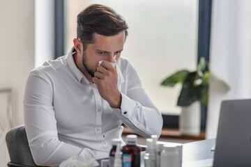 Ailing Young Businessman Sick with Cold or Flu, Working at Office Desk, Blows His Nose
