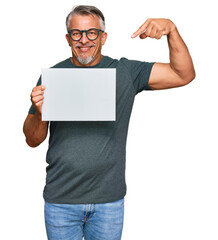 Middle age grey-haired man holding blank empty banner pointing finger to one self smiling happy and proud