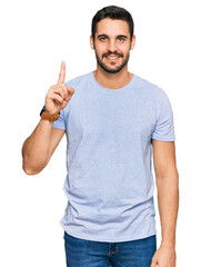 Young hispanic man wearing casual clothes pointing finger up with successful idea. exited and happy. number one.