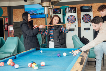 Group of cheerful friends playing pool