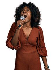 African woman with curly hair singing song using microphone angry and mad screaming frustrated and...