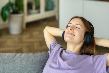 Happy young woman with headphones immersed in her thoughts while listening to her favorite music sitting on the couch at home