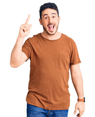 Young hispanic man wearing casual clothes pointing finger up with successful idea. exited and happy. number one.