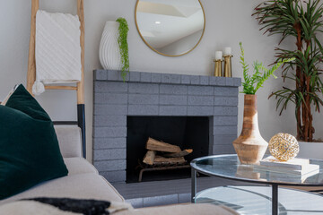 Living room scene of blue-gray painted brick fireplace with gold and wood accent pillows, vases, and natural greenery.