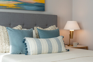 Relaxing bedroom detail of blue and white pillows on bed with gray headboard and decorative gold side lamp.