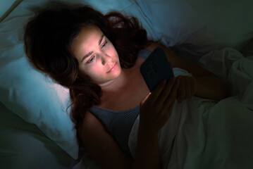 In the dim night, a woman lies in bed, absorbed in her phone's light, an illustration of insomnia...