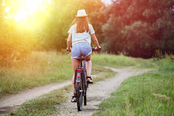 Young happy woman in a casual wear rides a bicycle in summer meadow. Beautiful girl enjoys summer nature. Relax, rest, nature concept.