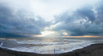 Aerial view of a young woman standing on a black beach on the surf line. summer day, rainy clouds. Sunset. Coast of Ureki beach, Georgia © Sergey