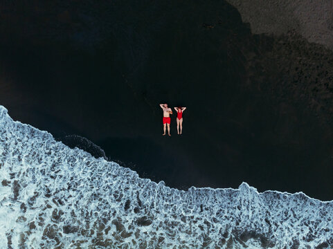 Black sand beach. Fantastic landscape of black sand volcano Ureki beach in Georgia. Couple having a good time on vacation. A man and a woman in red swimsuits are lying down