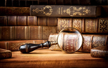 Old books and antique magnifying glass on a wooden background. An ancient book and magnifying glass...