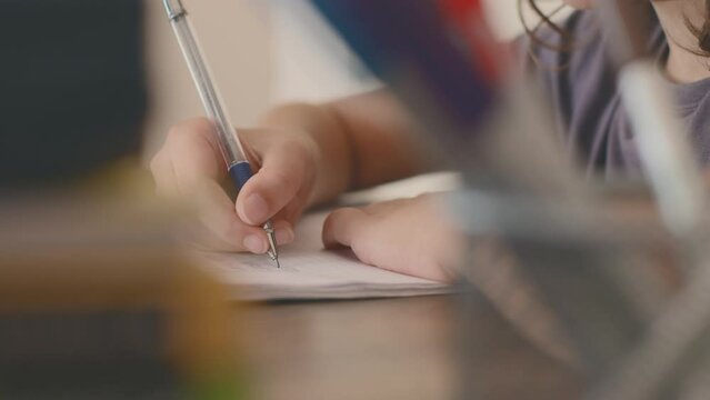 Side view of a concentrated little boy learning to write while doing his homework while sitting at his desk at home. hand close up. Portrait of a smart preschooler who is learning to write.
