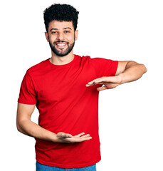 Young arab man with beard wearing casual red t shirt gesturing with hands showing big and large size sign, measure symbol. smiling looking at the camera. measuring concept.
