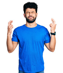 Fototapeta premium Young arab man with beard wearing casual blue t shirt gesturing finger crossed smiling with hope and eyes closed. luck and superstitious concept.