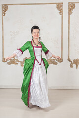 Beautiful happy woman in rococo style medieval dress dancing in the room