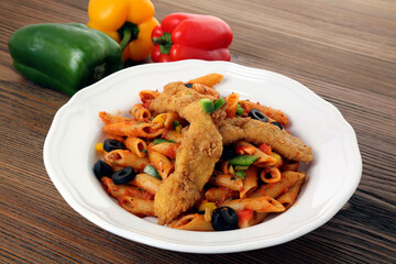 Crispy chicken pasta with bell pepper, back olive and cucumber served in dish isolated on table side view of arabic food