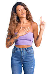 Young hispanic woman with tattoo wearing casual clothes smiling swearing with hand on chest and...