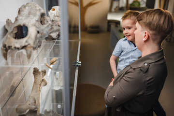 Woman holding her little son in front of the showcase with animal skeleton and skull during a...