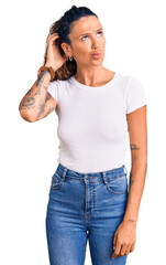 Young hispanic woman with tattoo wearing casual white tshirt confuse and wondering about question....