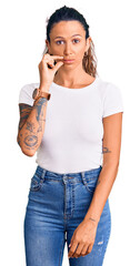 Young hispanic woman with tattoo wearing casual white tshirt mouth and lips shut as zip with...