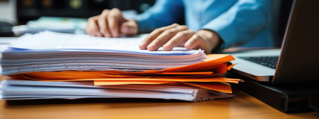 Close-up of a man working with a stack of documents and reports on his office desk - obrazy, fototapety, plakaty