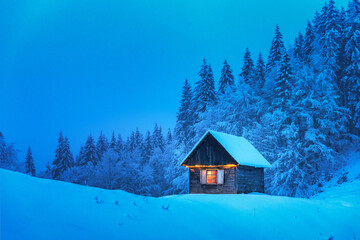 A lonely wooden house surrounded by snowy pine trees in a mountain glade deep within the woods in a wintery landscape. Christmas holiday postcard. Snowy mountains forest