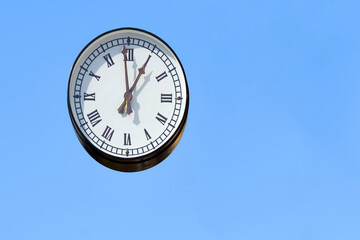Street round clock with Roman numerals on a blue clear sky