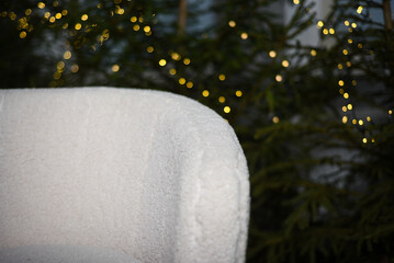 white corner of the sofa near green fir trees with Christmas lights that create a bokeh effect.