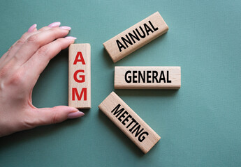 AGM - Annual general meeting symbol. Concept word AGM on wooden blocks. Businessman hand. Beautiful...