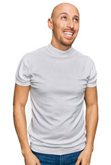 Bald man with beard wearing casual white t shirt looking away to side with smile on face, natural expression. laughing confident.