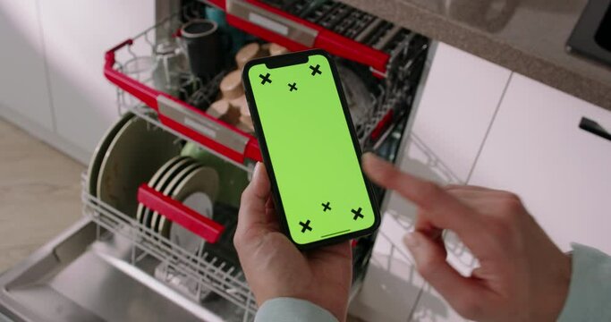 Woman hold smartphone with chroma key against the background of an open dishwasher. Tap at bottom, placing and paying for order in online store. Mobile app advertisement. Online shopping, technologies