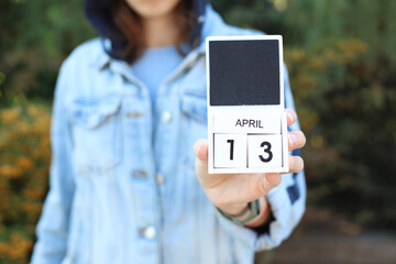 Woman in denim jacket holds white block wooden calendar with date April 13 outdoors